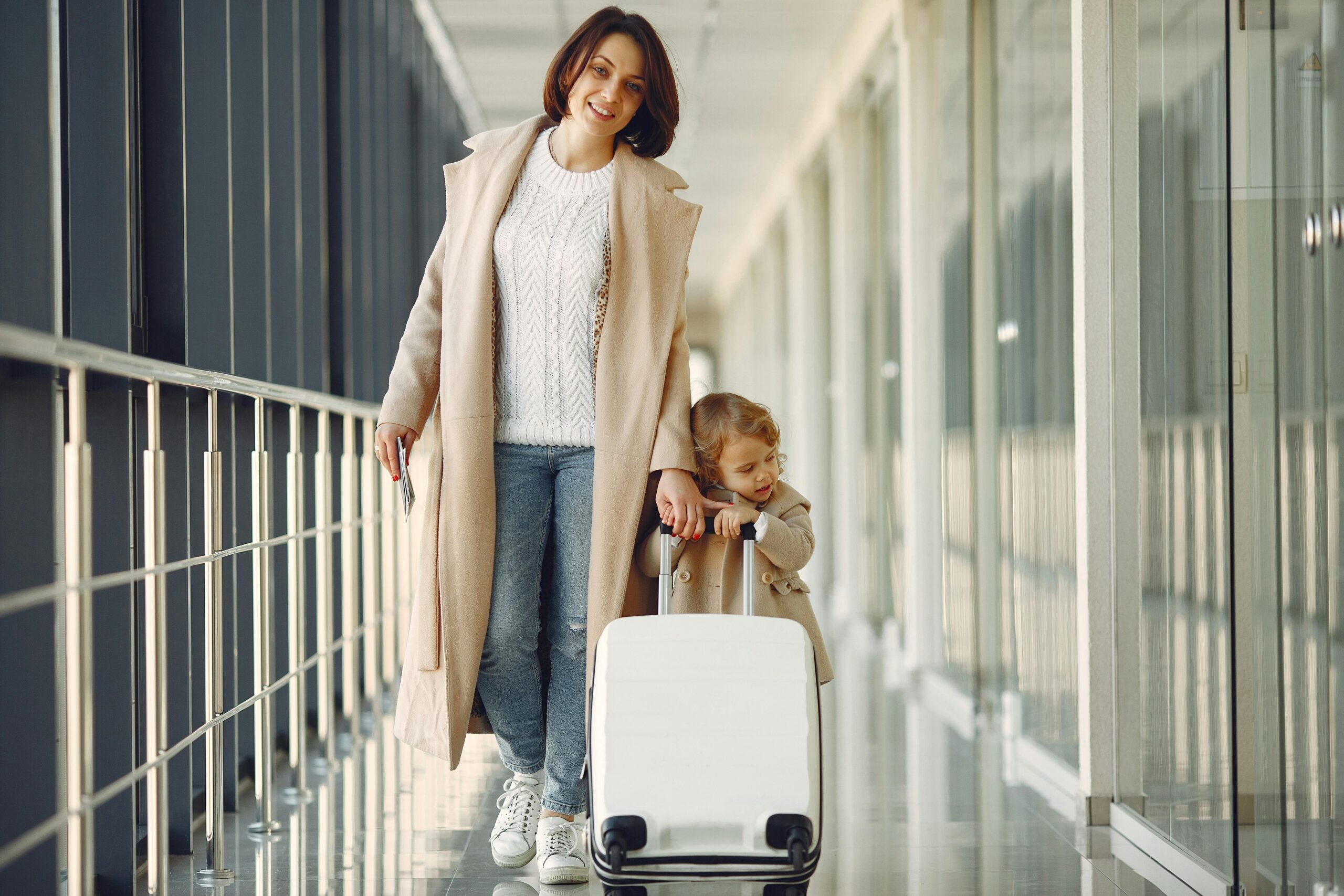 Mother and daughter walking together in an airport corridor with a suitcase