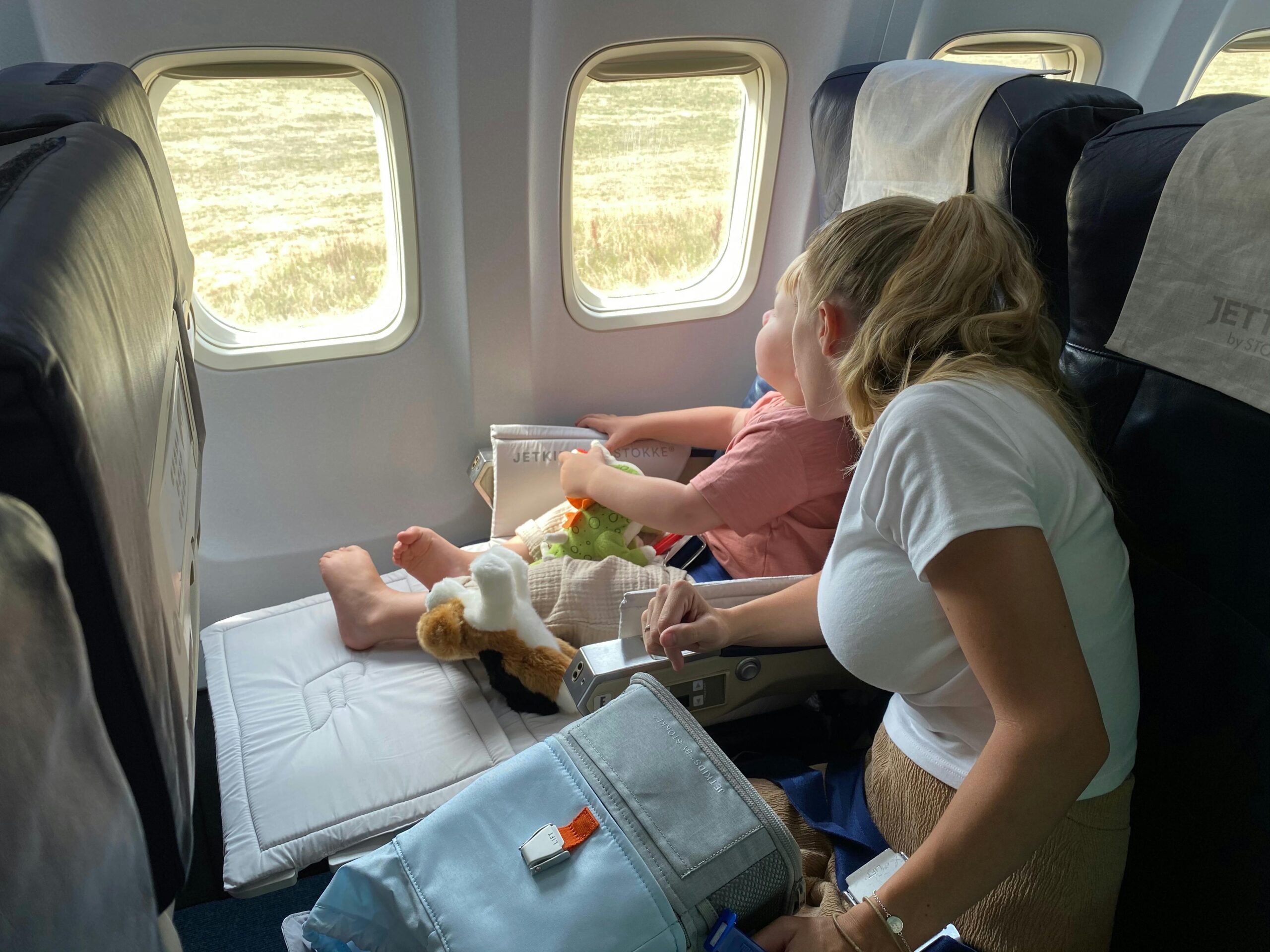Mother helping her toddler settle into an airplane seat by the window